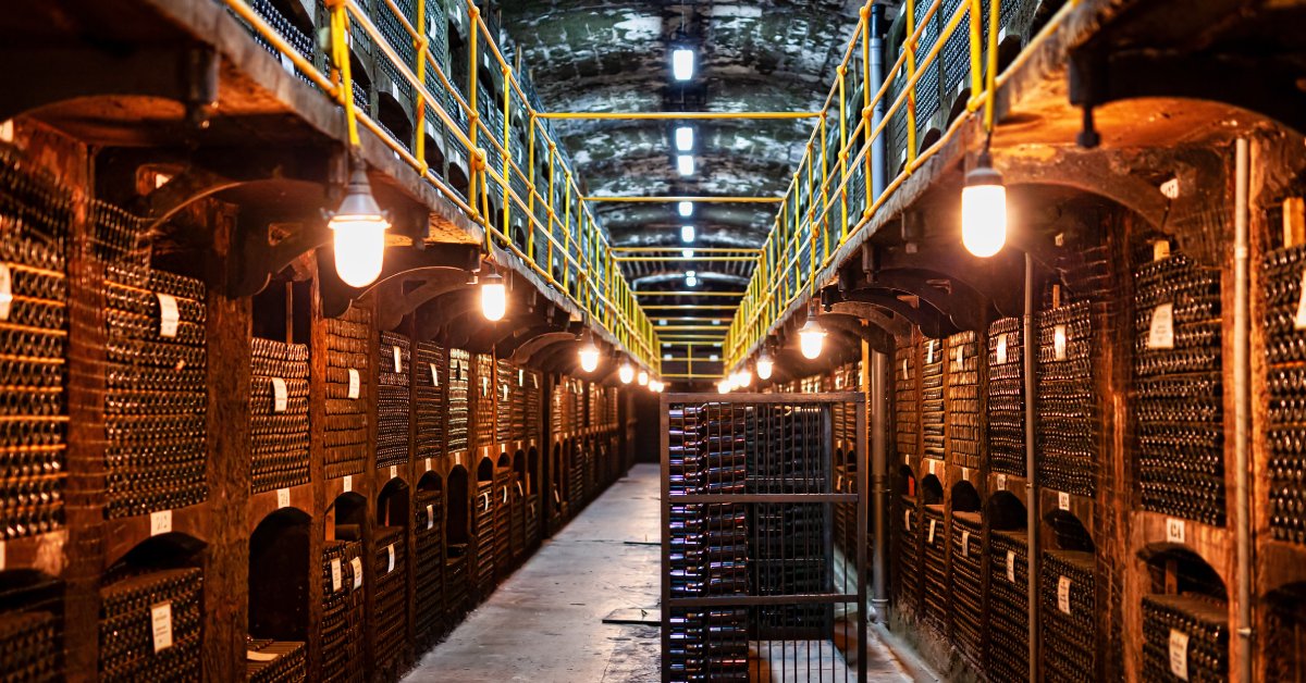 A large, modern wine storage facility. There are wine bottles stacked on either side of a pathway through the center.