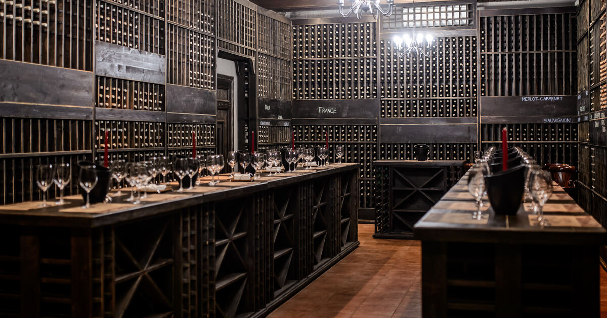 A large wine storage room with clay tile flooring and dark wood shelving units full of horizontally-stored wine bottles.