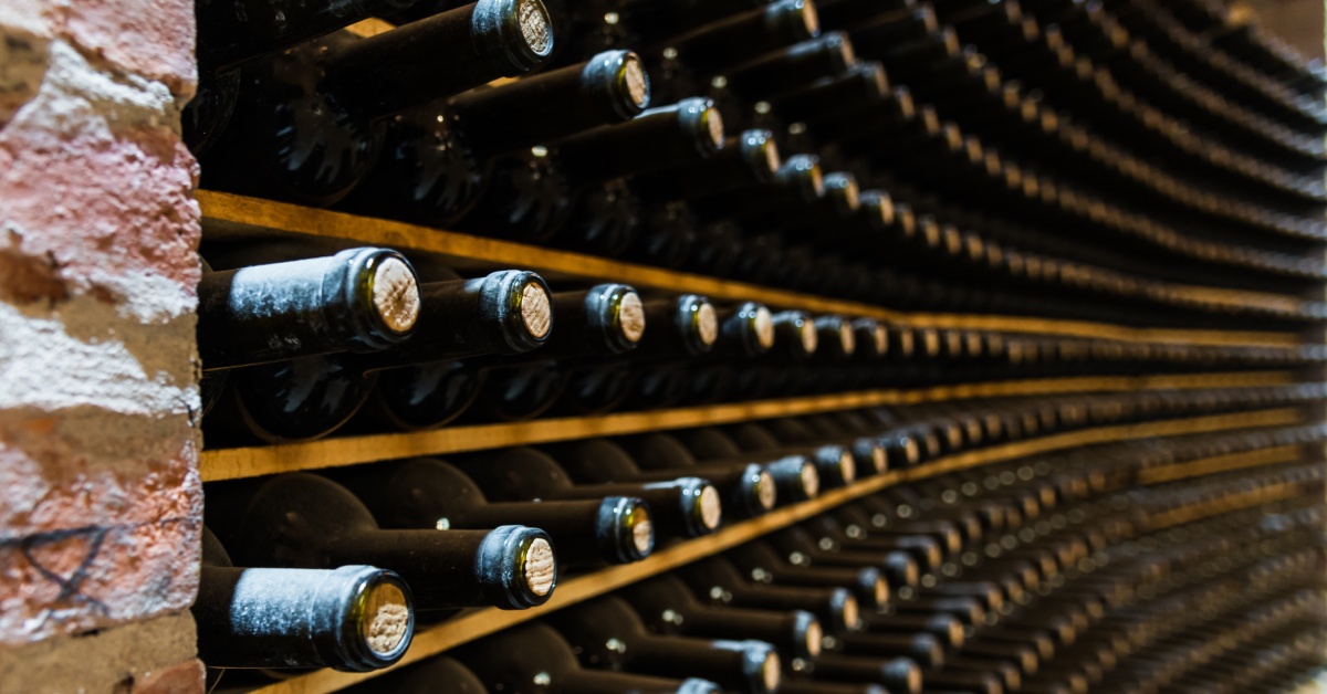 A wine cellar with horizontally stored wine bottles on brick shelves across from large wine barrels.