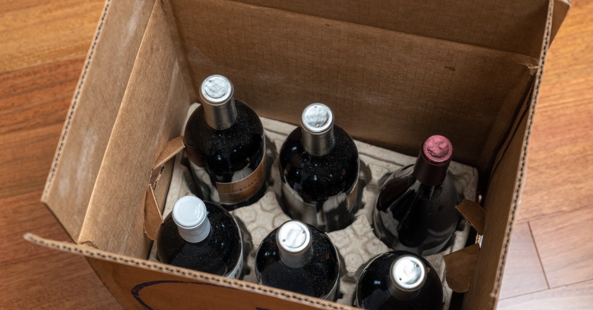 Six bottles of wine sitting in an open cardboard box with a bottle tray holder at the bottom of the box.