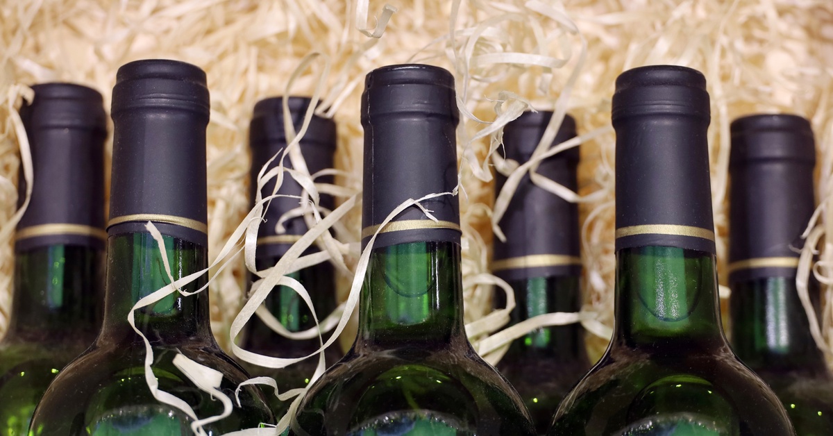 A collection of dark, emerald green wine bottles sit comfortably stacked in paper shreds for transport.