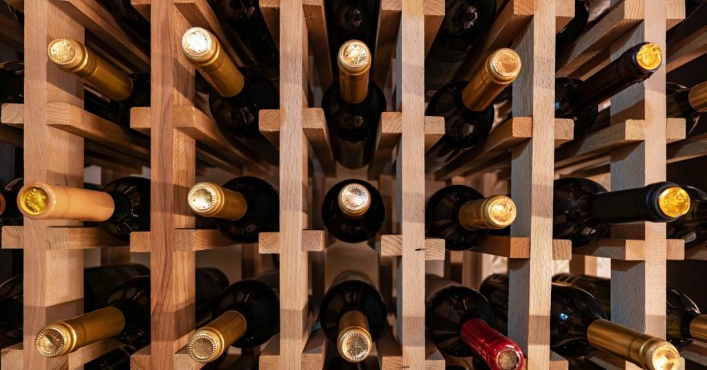 A collection of wine bottles arranged in light-brown wooden shelves with the tops of the bottles facing out.
