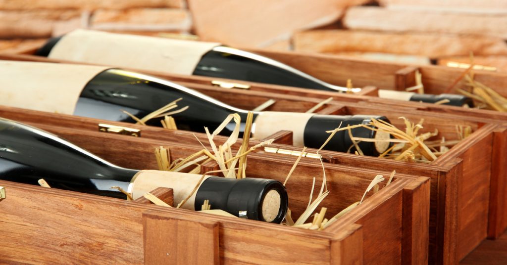 Bottles of red wine resting in wooden boxes on top of hay to cushion them during transportation.