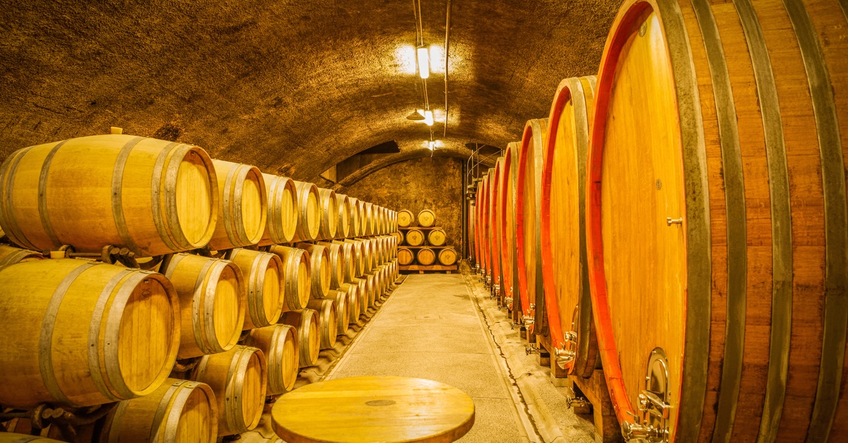 A warmly lit constant-temperature arched cellar with French barrique oak barrels used to age wine.